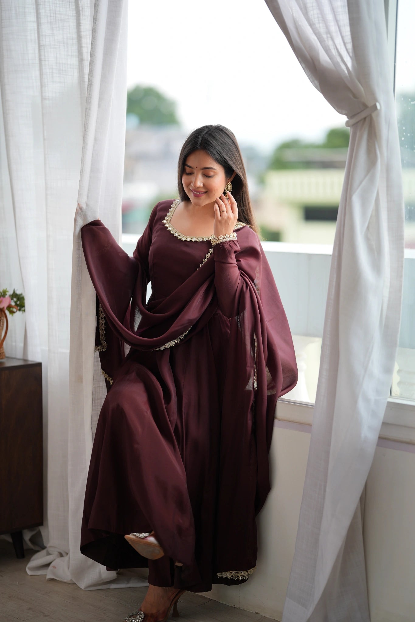 Dark Brown Anarkali suit seated pose with dupatta by the window